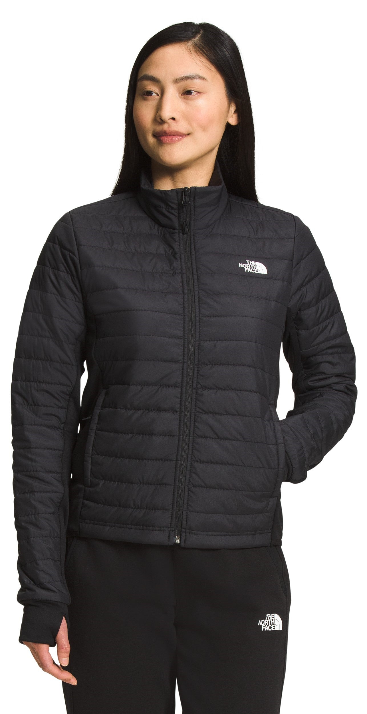 A woman wearing a black quilted jacket and black sweatpants.