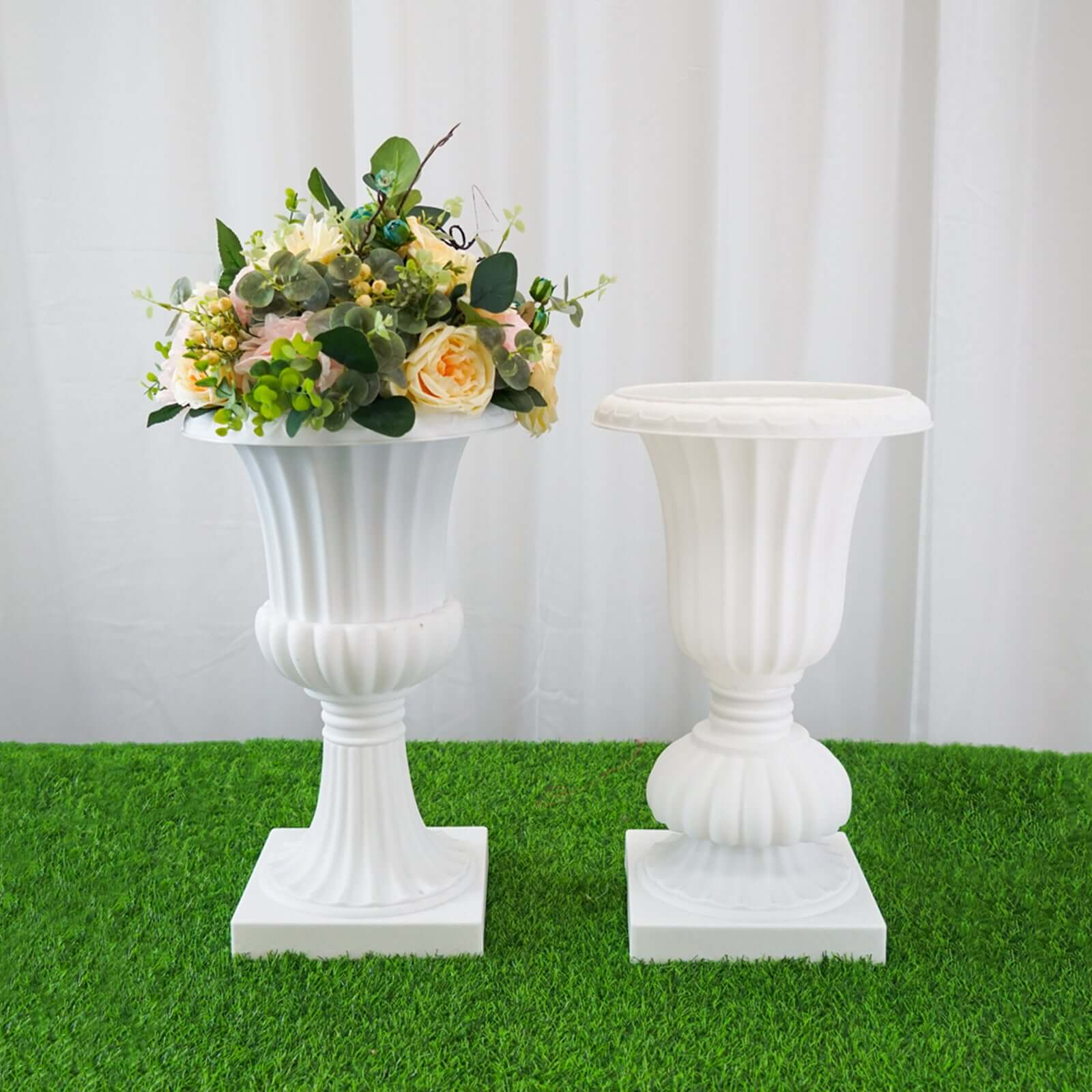 White decorative urns with flowers on a green grass surface.