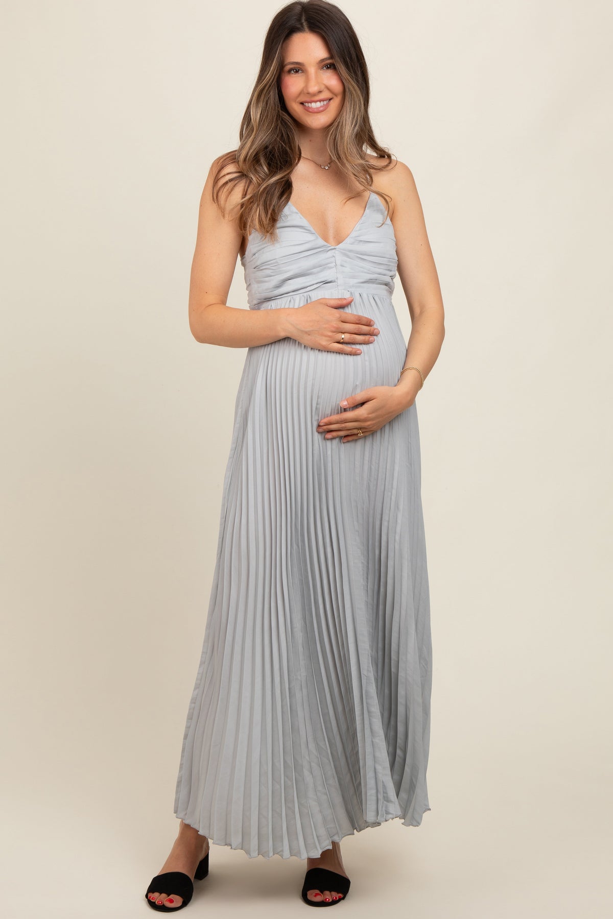 woman wearing a light gray pleated maternity maxi dress and holding her baby bump