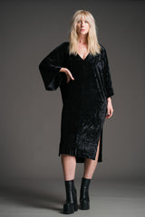 Sara wears Little Lies Rumours black velvet midi dress with wide sleeves and V‑neckline, styled with black platform boots in a studio full‑length front view.